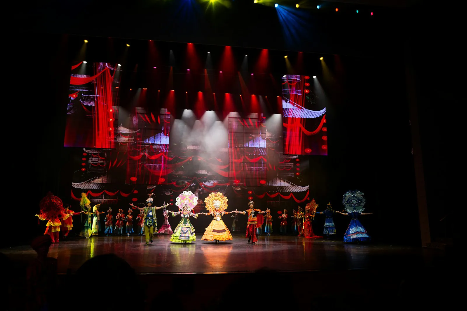 Students in bright costumes performing on the auditorium stage under coloured lights