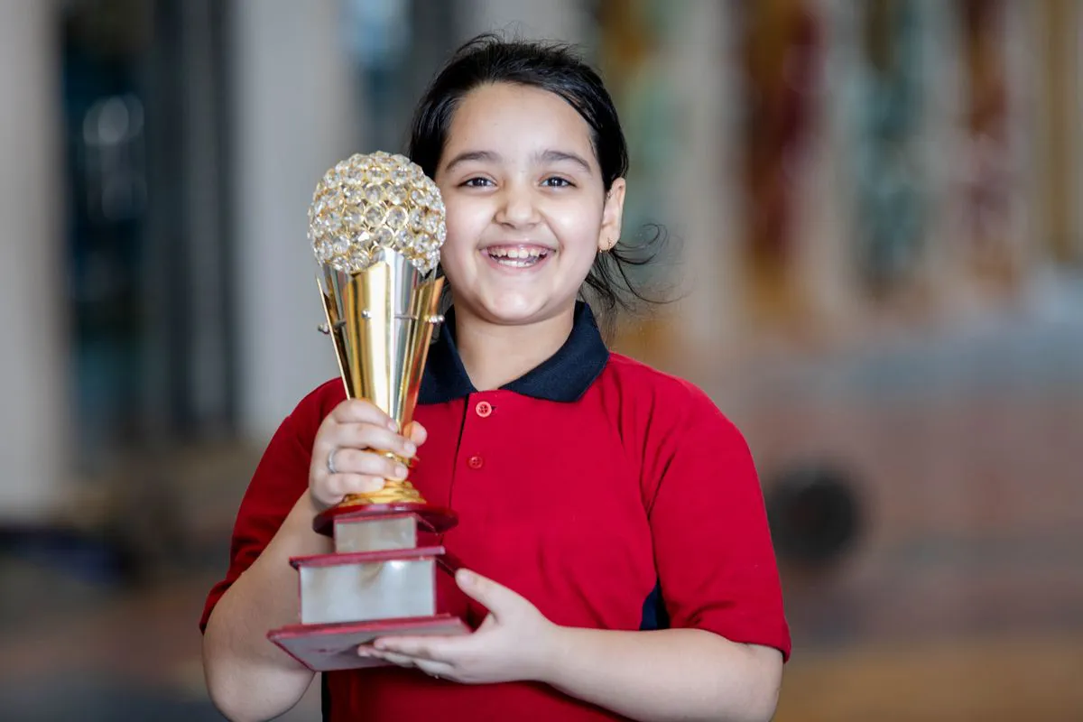 A smiling student holding up a gold trophy