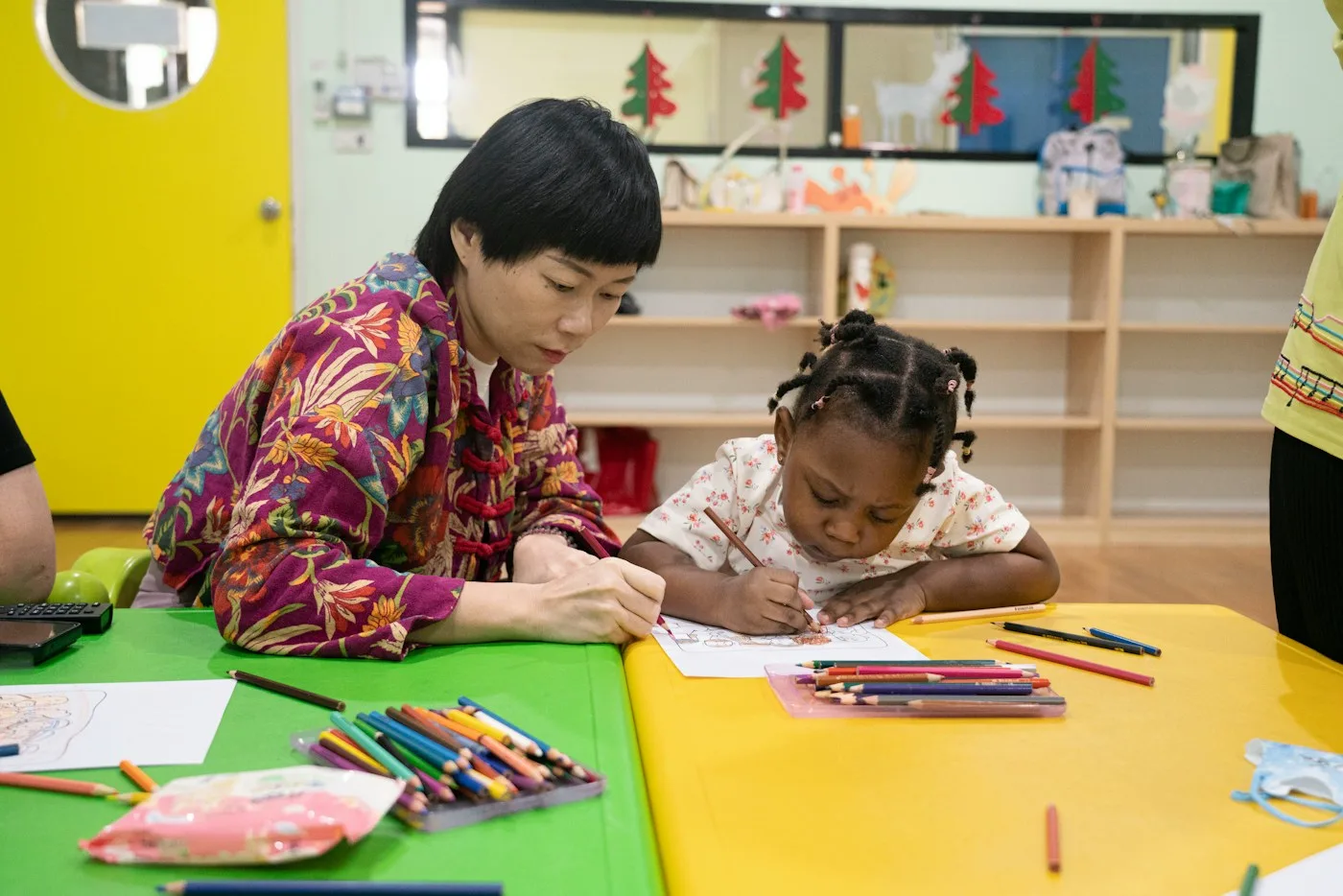 A teacher drawing at a low table beside a small child