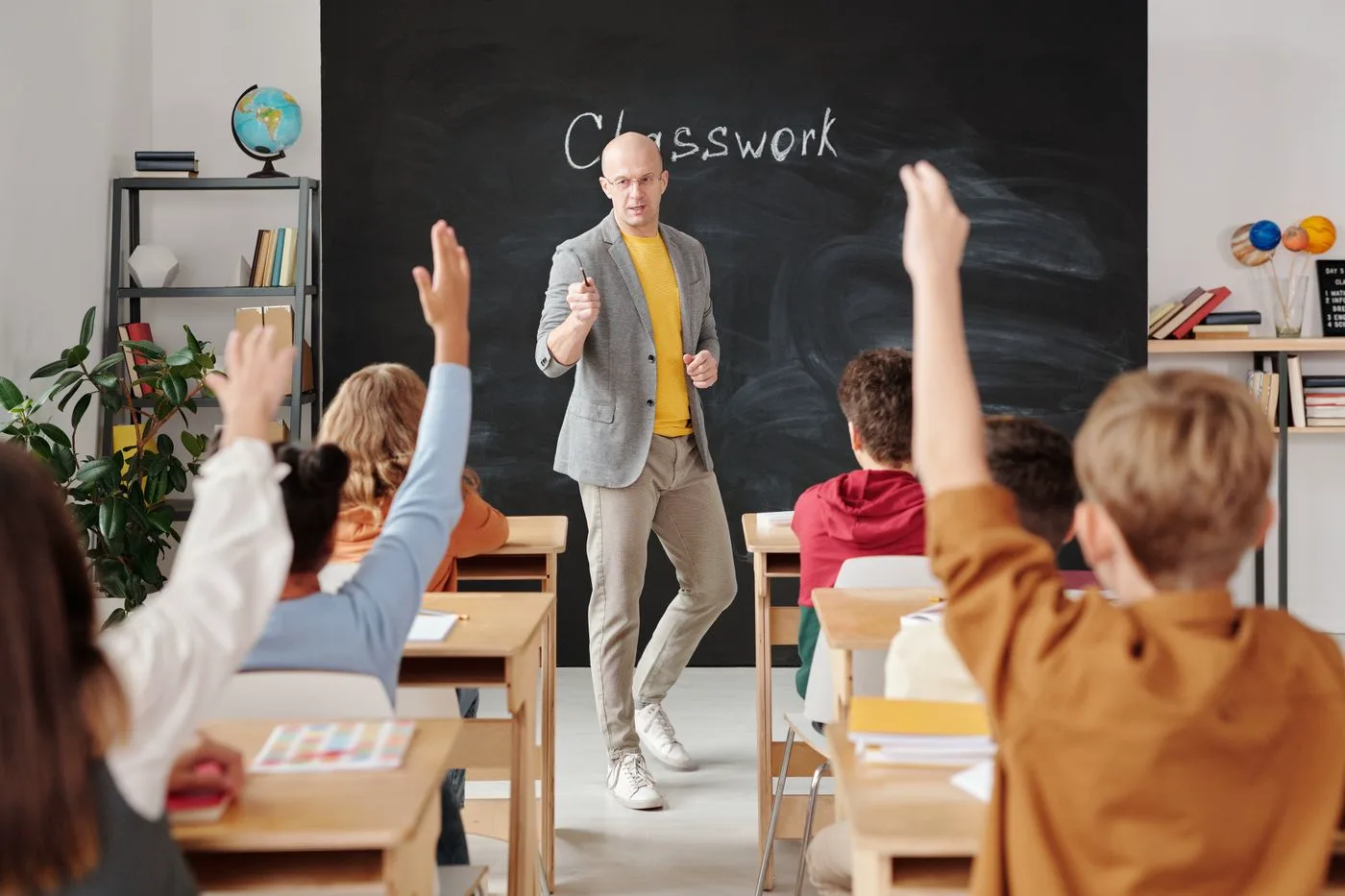 Children raising their hands for a teacher in a primary classroom