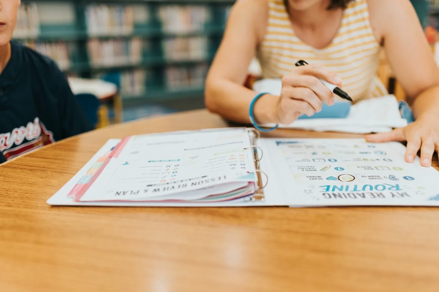 A student writing notes in an open binder beside a teacher